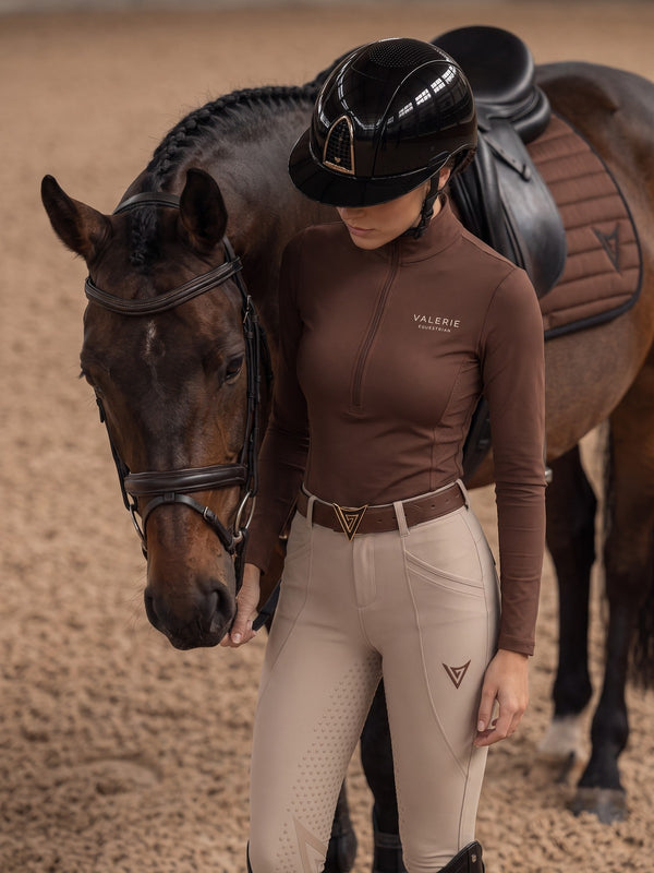 Rider in beige competition breeches standing beside a bay horse in an arena — Valerie Equestrian Impulsion