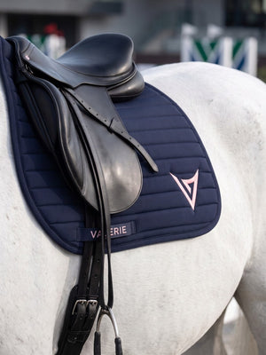 Navy nylon jumping saddle pad with pink V logo under saddle on grey horse — Valerie Equestrian Devotion