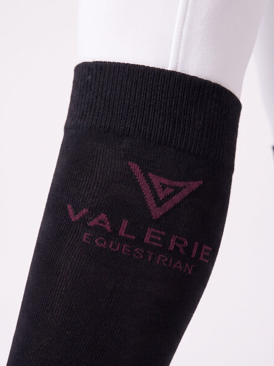 Black riding knee-highs with burgundy logo, worn with white breeches, side view — Valerie Equestrian Support